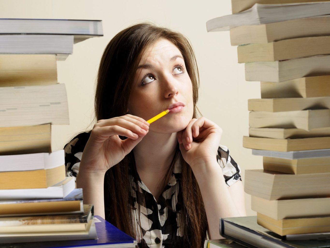 Video lezioni online tedesco ragazza che pensa con matita in bocca circondata da libri ragazza che pensa con matita in bocca circondata da libri